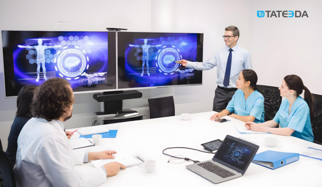 A healthcare IT consultant leading a presentation in a conference room, showcasing advanced digital health technologies on large screens to medical professionals. Highlights what to look for in a healthcare IT consultant for effective healthcare IT collaboration. | TATEEDA